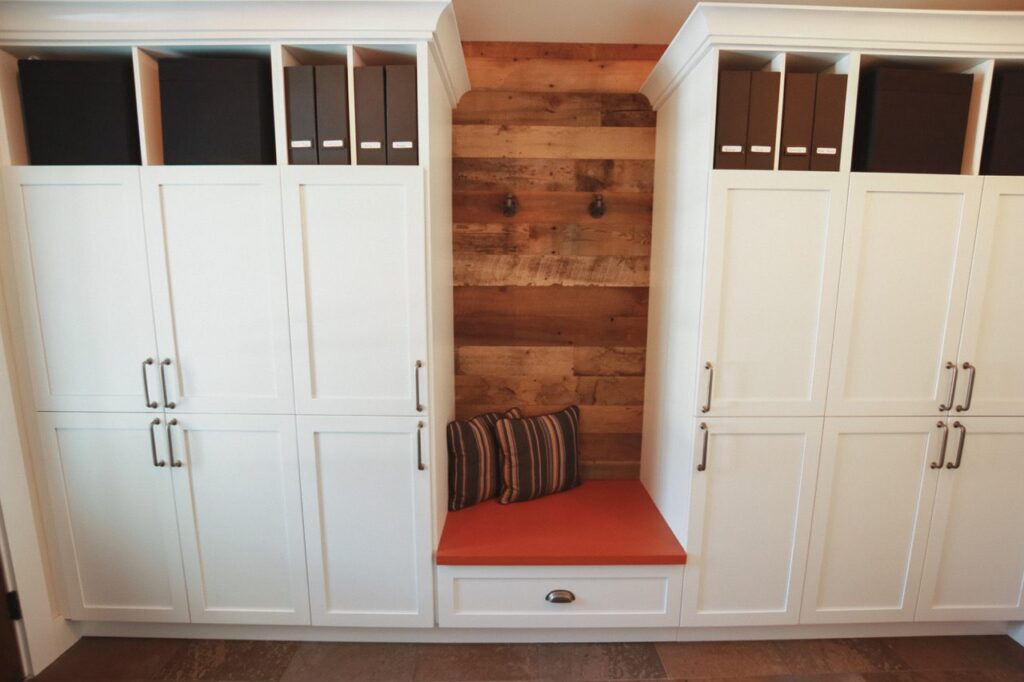 Mudroom bench niche lined with brown reclaimed wood planks between white built-in cabinets