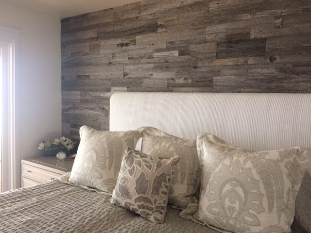 Grey reclaimed wood bedroom wall behind an upholstered headboard